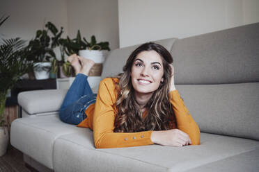 Thoughtful woman with hand in hair lying on sofa at home - EBBF04945