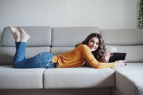 Frau mit Tablet-PC zu Hause auf dem Sofa liegend - EBBF04953