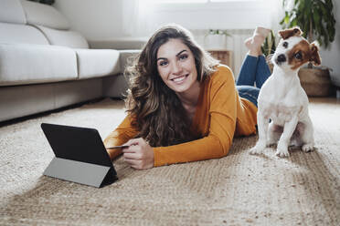 Frau mit Tablet-PC auf dem Boden liegend mit Hund zu Hause - EBBF04957