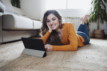 Smiling woman watching tablet PC lying on floor at home - EBBF04960