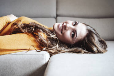 Smiling woman lying on sofa at home - EBBF04964