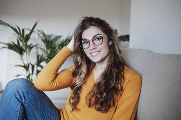 Woman with hand in hair sitting on sofa - EBBF04968