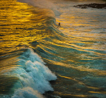 Ein Surfer erwischt eine Welle in den goldenen Reflexen des Sonnenuntergangs an der Südküste von Kauai, Hawaii, Vereinigte Staaten von Amerika, Pazifik - RHPLF21167