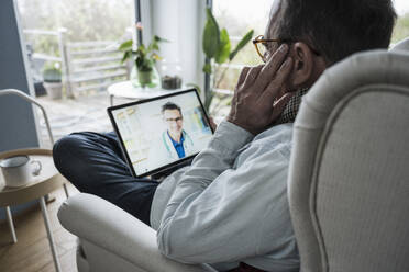 Man discussing with doctor on video call through tablet PC at home - UUF25234