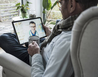 Smiling doctor on video call through digital tablet talking with man having coffee at home - UUF25235