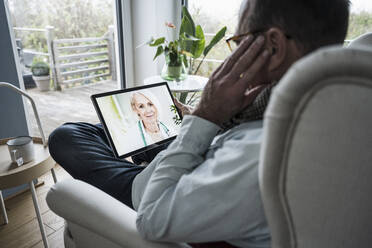 Smiling doctor on tablet PC screen talking with man at home - UUF25236