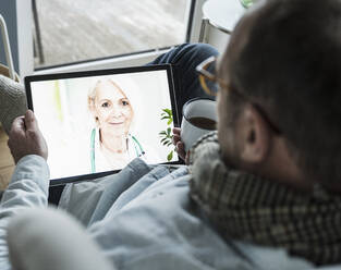 Doctor advising patient on video call through digital tablet at home - UUF25237