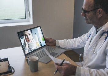 Patient im Gespräch mit einem Arzt, der einen Bericht am Schreibtisch in der Klinik hält - UUF25246