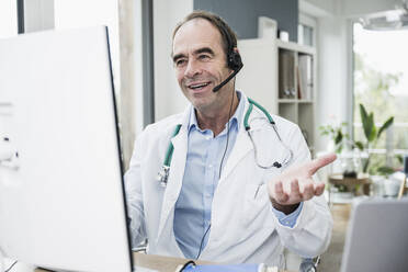 Lächelnder Arzt gestikuliert bei Videoanruf in der Klinik - UUF25248