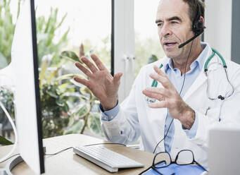 Arzt spricht über Headset bei einem Videoanruf im Büro - UUF25250
