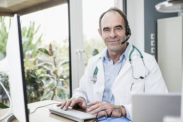 Smiling doctor wearing headset sitting at clinic - UUF25251