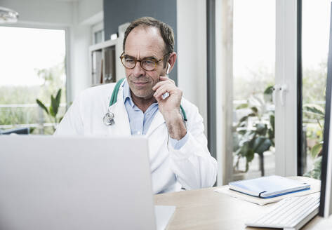 Arzt mit Laptop, konzentriert am Schreibtisch in der Klinik - UUF25254