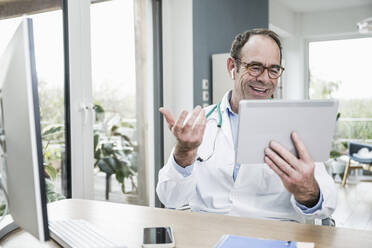 Happy doctor with digital tablet gesturing on video call at hospital - UUF25255