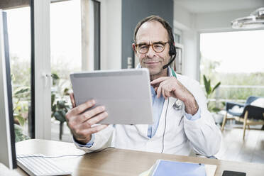 Smiling doctor on video call through tablet PC at medical clinic - UUF25261