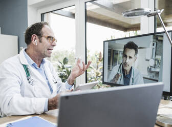Doctor talking with colleague on video call through computer in clinic - UUF25264