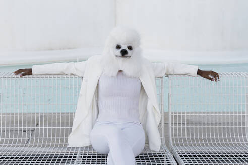 Entspannte Frau mit weißer Hundemaske sitzt auf einer Bank - JRVF02184