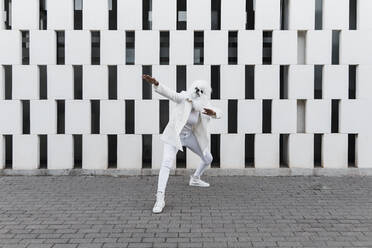 Woman wearing dog mask dancing in front of wall - JRVF02193