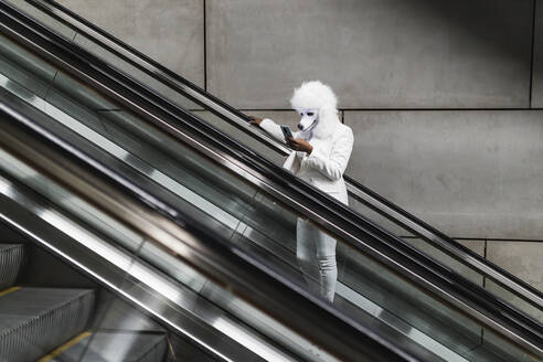 Frau mit Hundemaske benutzt Mobiltelefon auf Rolltreppe - JRVF02215