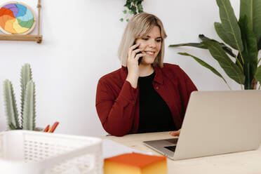 Smiling businesswoman talking on smart phone working on laptop - TCEF02099