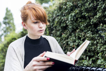 Junge Frau liest Buch an einer Hecke - WPEF05562