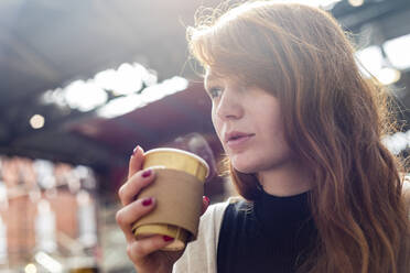 Young woman having coffee in disposable cup at cafe - WPEF05566