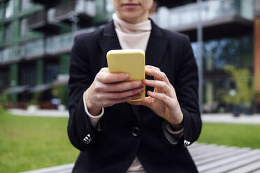 Geschäftsfrau sitzt auf einer Bank im Büropark und benutzt ein Mobiltelefon - ASGF01832