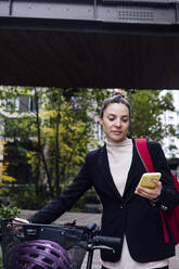 Businesswoman with electric bicycle using mobile phone - ASGF01837