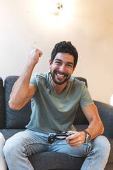 Cheerful man with joystick playing video game at home - JAQF01003