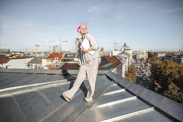 Frau mit Laptop und Kopfhörern auf dem Dach stehend - AANF00225