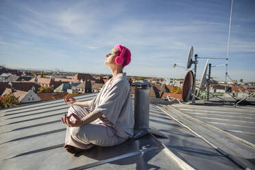 Frau mit Kopfhörern beim Meditieren auf dem Dach - AANF00228