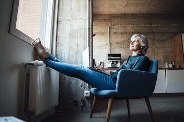 Thoughtful businesswoman with laptop on armchair in office - JOSEF05997