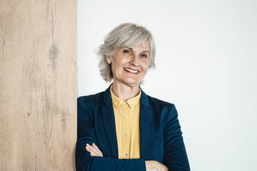 Smiling businesswoman with arms crossed in front of wall - JOSEF06010