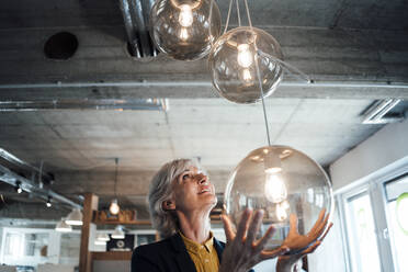 Senior businesswoman looking at pendant light in office - JOSEF06013