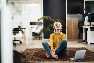 Geschäftsfrau übt Yoga am Laptop auf dem Teppich im Büro - JOSEF06018