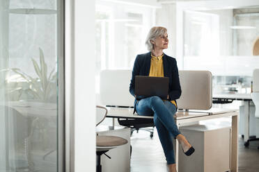 Businesswoman sitting with laptop on desk - JOSEF06021