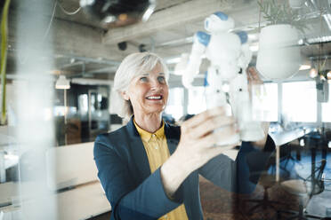 Ältere Geschäftsfrau hält Roboterspielzeug im Büro - JOSEF06027
