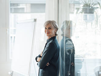 Senior businesswoman with arms crossed leaning on glass wall - JOSEF06035
