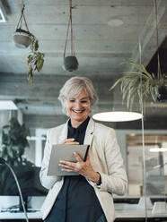 Smiling senior businesswoman using tablet PC at office - JOSEF06040