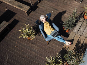 Businesswoman with hands behind head resting on armchair at rooftop - JOSEF06043