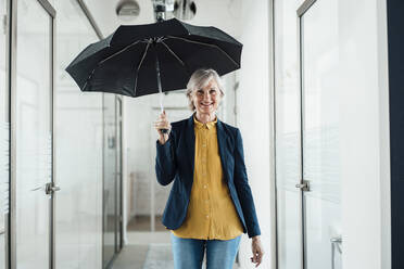 Lächelnde Geschäftsfrau mit Regenschirm im Büroflur - JOSEF06083