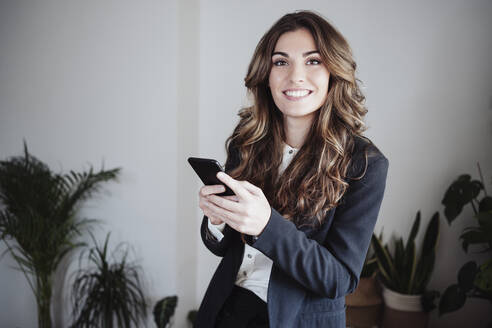 Lächelnde Geschäftsfrau mit Mobiltelefon im Büro - EBBF04990