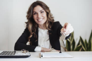 Smiling saleswoman holding house keys at office - EBBF05000