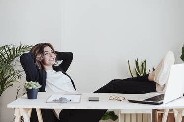 Working woman with hands behind head relaxing at office - EBBF05022