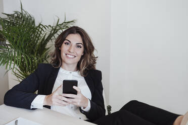 Arbeitende Frau mit Smartphone lächelt im Büro - EBBF05025