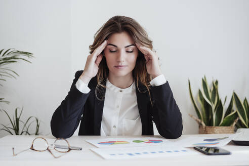 Müde Geschäftsfrau mit Kopf in den Händen sitzt am Schreibtisch im Büro - EBBF05029