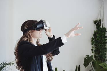 Young businesswoman gesturing wearing virtual reality headset at office - EBBF05065