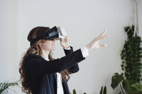 Junge Geschäftsfrau gestikuliert mit Virtual-Reality-Headset im Büro - EBBF05065