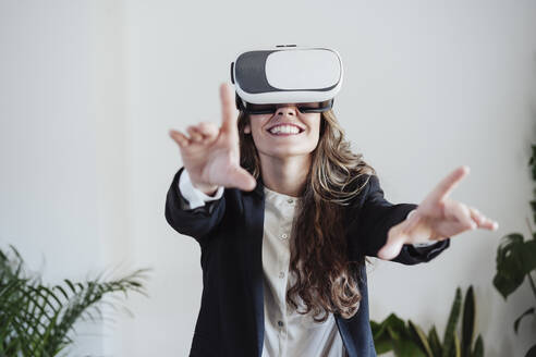 Lächelnde Geschäftsfrau, die mit einem Virtual-Reality-Headset im Büro gestikuliert - EBBF05066