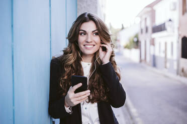Geschäftsfrau hört Musik auf einem Smartphone und lehnt sich an eine blaue Wand - EBBF05073