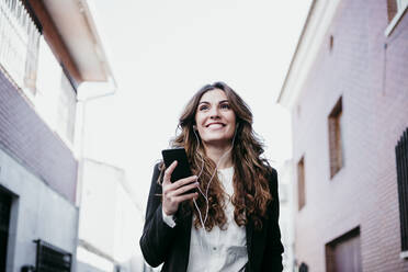 Smiling businesswoman listening music on smart phone - EBBF05077